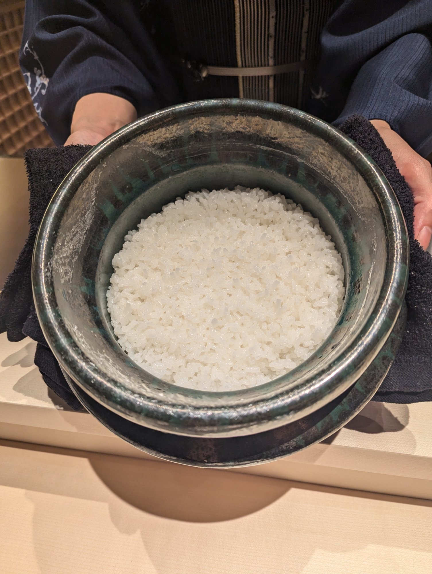 女将が両手で釜を持って運ぶ白米様。つやつやと炊き上がった米が見える